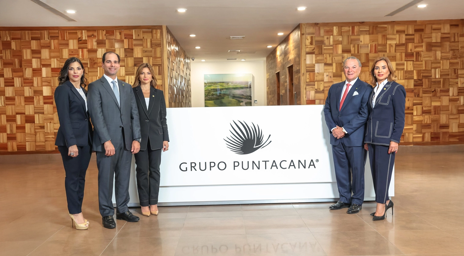 Cinco representantes de Grupo Puntacana posan en las instalaciones de la empresa, junto a un mostrador blanco con el logotipo corporativo, en un espacio de paredes revestidas de madera.
